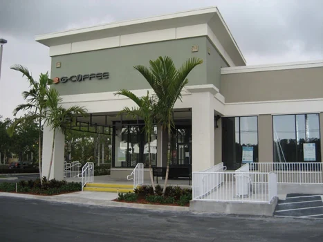 Café storefront with tall windows, palms, and a white terrace railing