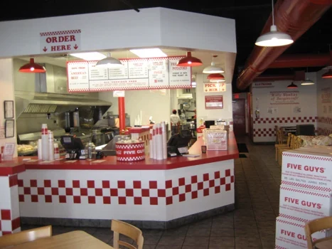 Five Guys ordering counter with red-and-white tile and overhead menus