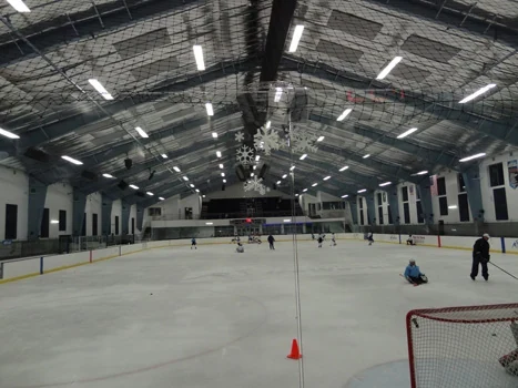 Indoor ice rink beneath a steel roof with suspended lighting