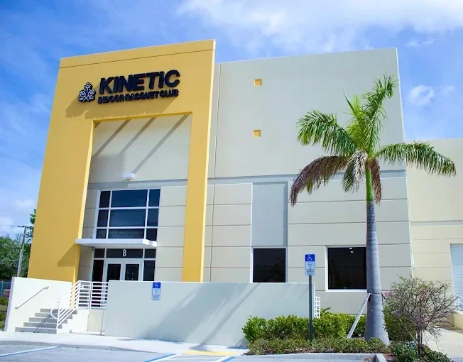 Kinetic Indoor Racquet Club entrance in Boynton Beach with yellow accents and palm trees