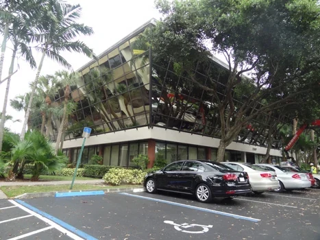 Office building with reflective windows, mature trees, and parking spaces
