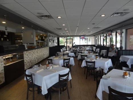 Restaurant dining room with white tablecloths, a long bar, and perimeter windows