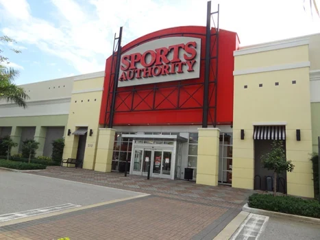 Sports Authority entrance with a red sign tower and landscaped walkway