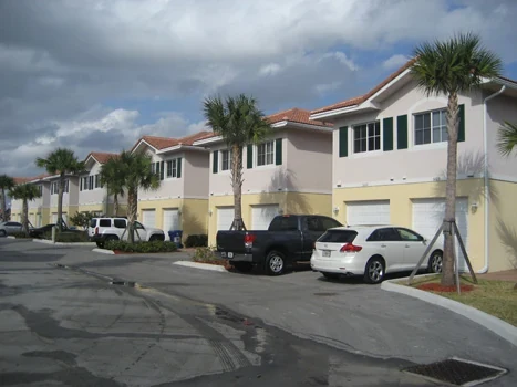 Townhouse streetscape with garage doors, parked vehicles, and palm trees