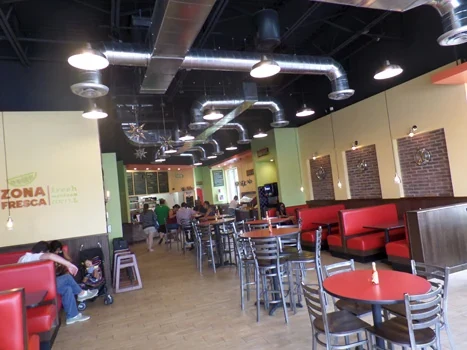 Zona Fresca dining room with exposed ducts, pendant lighting, and red seating